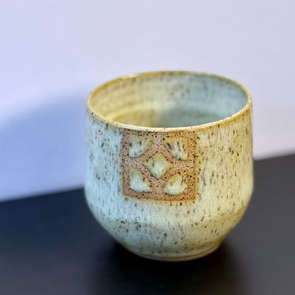 Handmade ceramic tumbler with a rounded shape and warm, yellow glaze. A square Empress breeze-block motif is inset on the front, revealing the natural clay and adding a mid-century geometric detail.