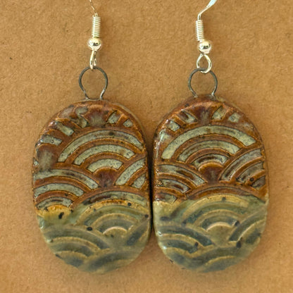 Pair of ceramic earrings with wave pattern on a brown background