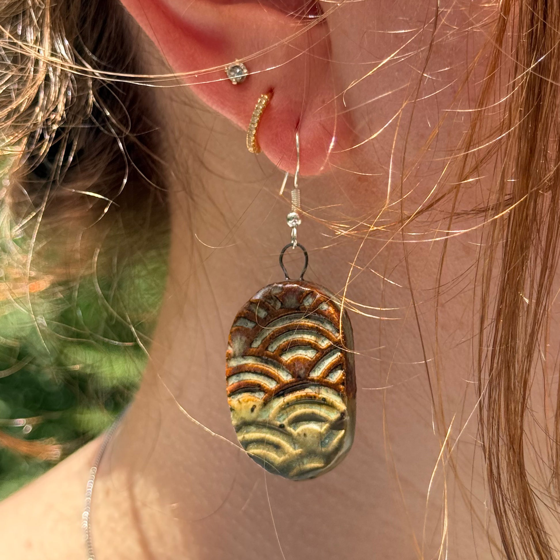 Close-up of a person wearing a textured earrings with a blurred natural background