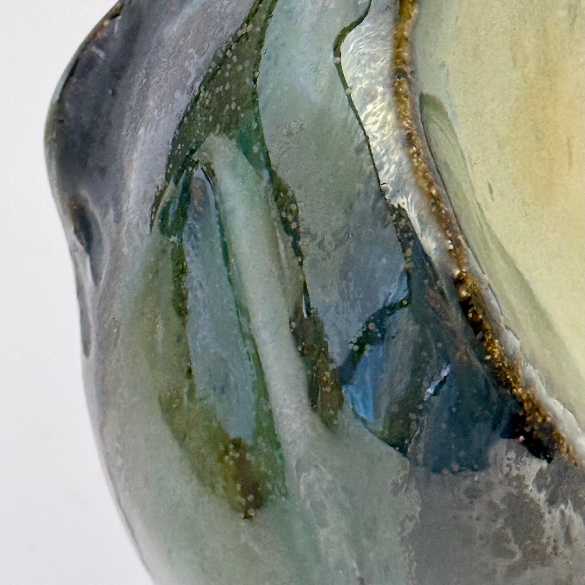 Close-up of handbuilt stoneware vase with a rounded organic form, textured surface impressions, and layered green and cream glaze. The sculptural piece stands on three small feet and has an earthy, natural finish.
