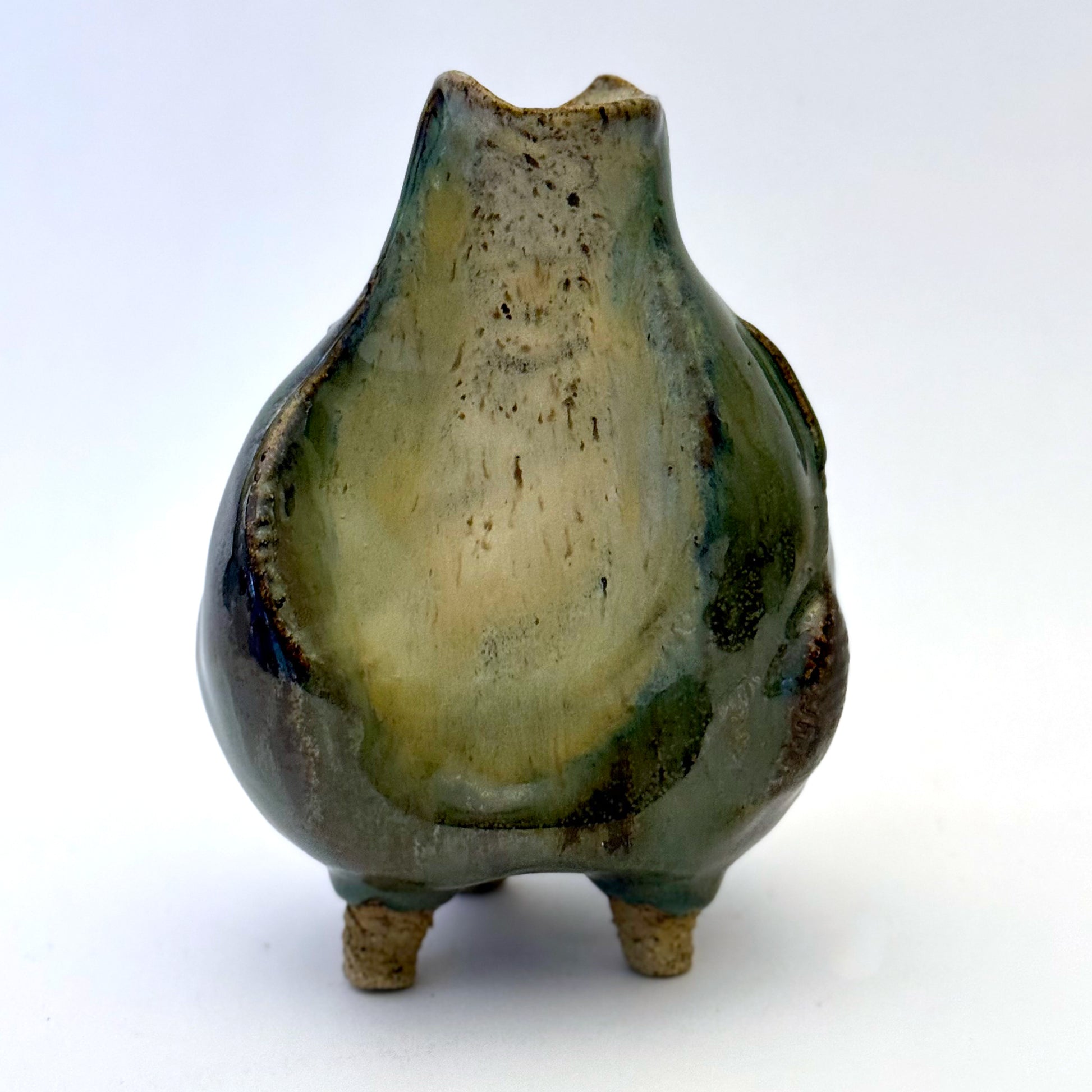 Handbuilt stoneware vase with a rounded organic form, textured surface impressions, and layered green and cream glaze. The sculptural piece stands on three small feet and has an earthy, natural finish.