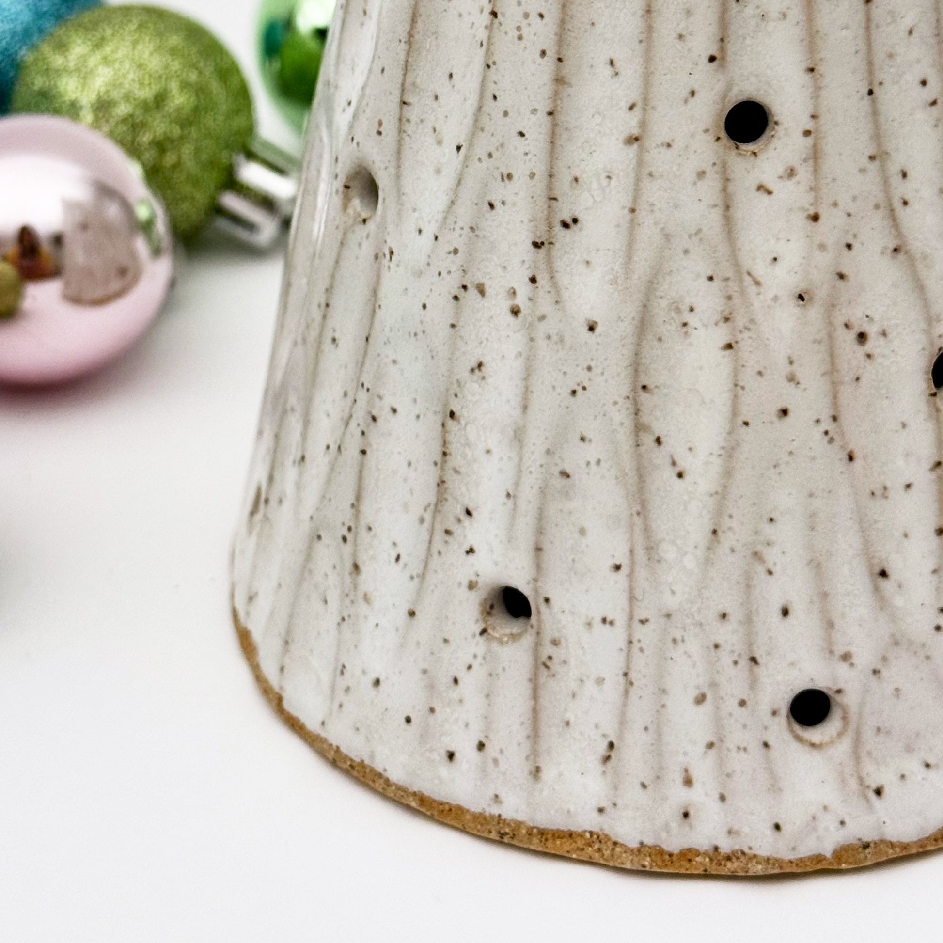 close-up of Speckled ceramic tree luminary with decorative Christmas ornaments in the background