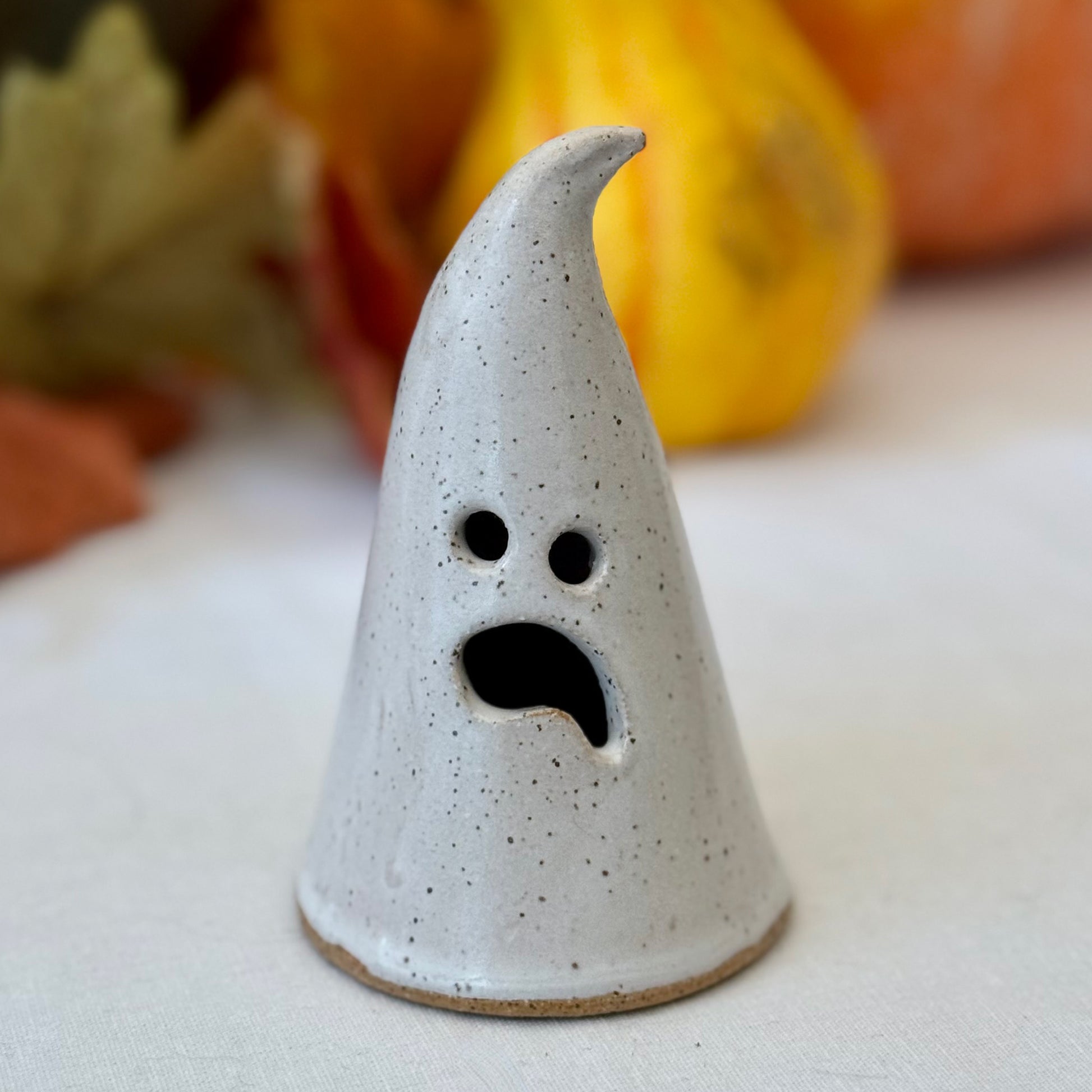 Ceramic ghost decoration with a surprised expression on a neutral background