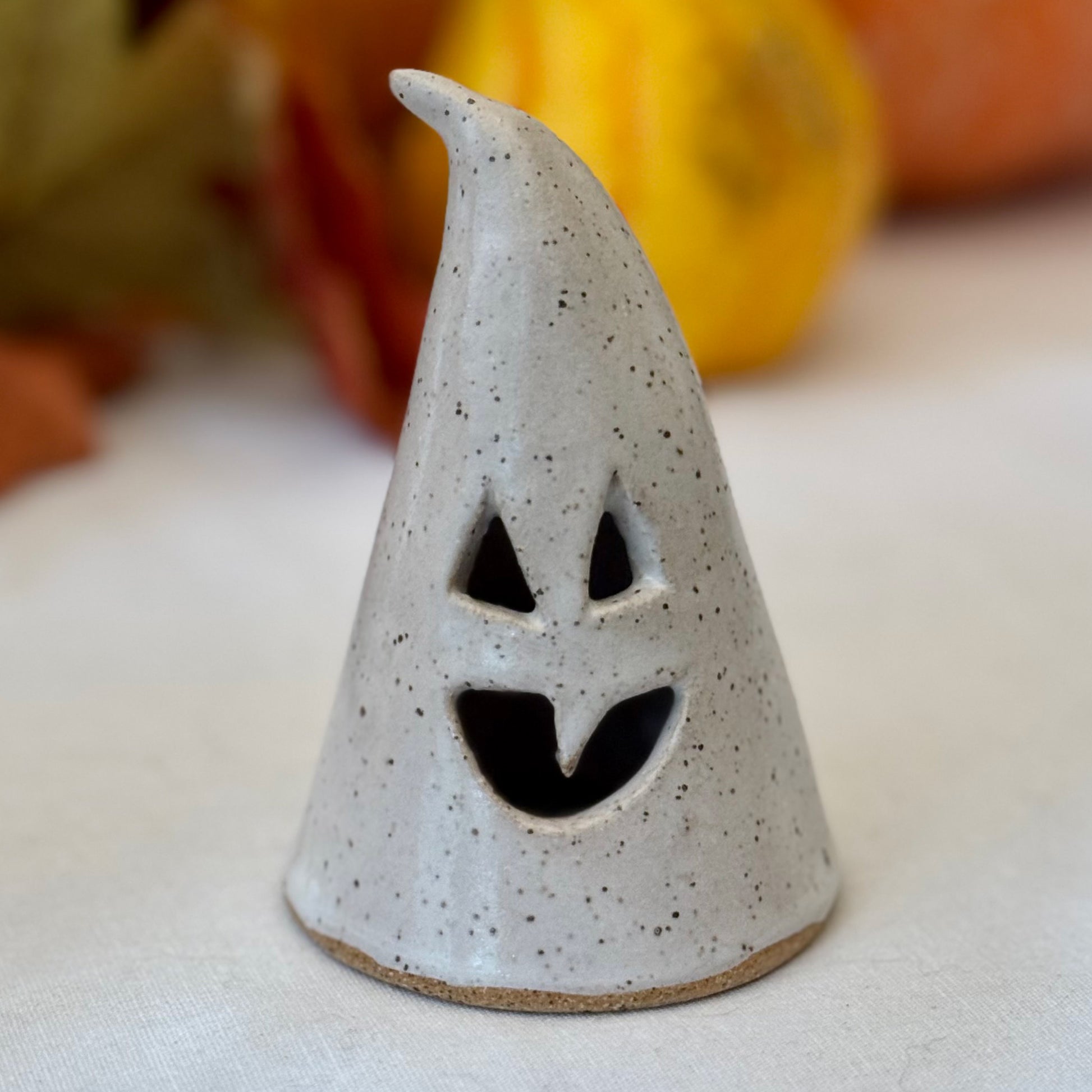 small ceramic luminary on a white surface with pumpkins in the background