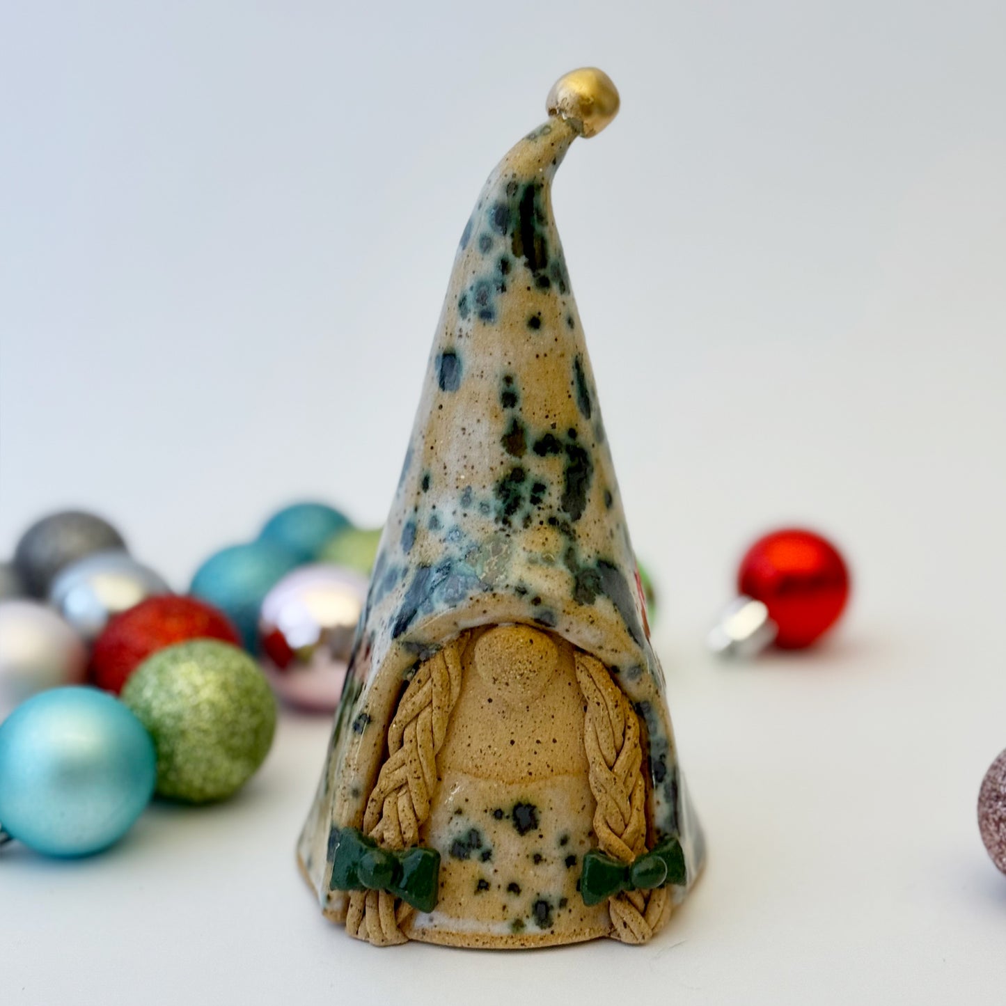 Decorative ceramic gnome figure with a pointed hat surrounded by colorful ornaments on a light background