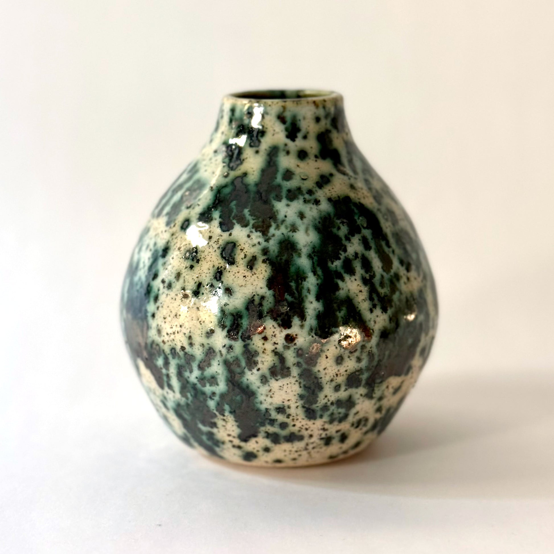 Small handmade pottery vase with a rounded shape and narrow opening, finished in a green jasper glaze with varied green tones and irregular speckled patterning across the surface.