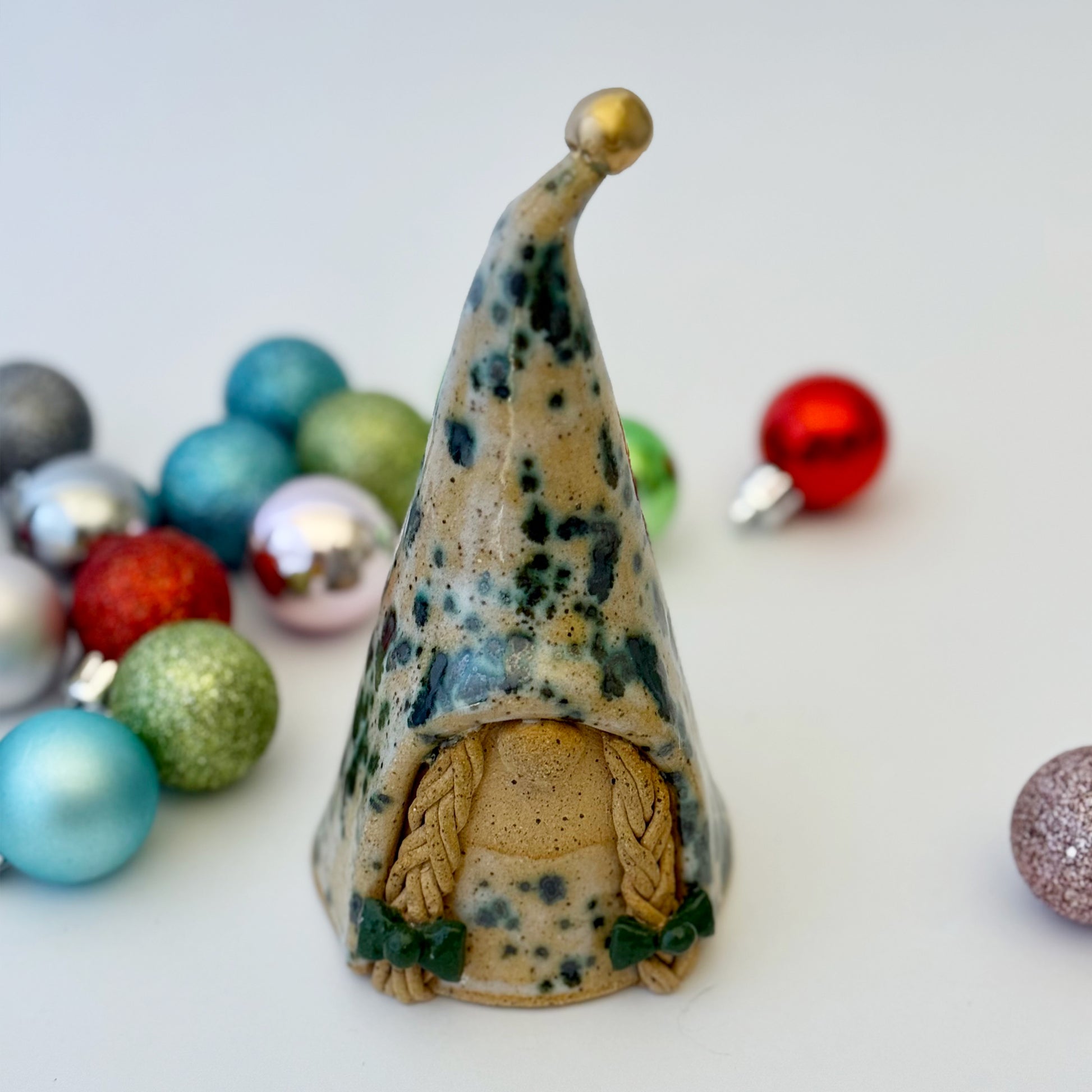 Decorative ceramic gnome figure with a pointed hat surrounded by colorful ornaments on a light background