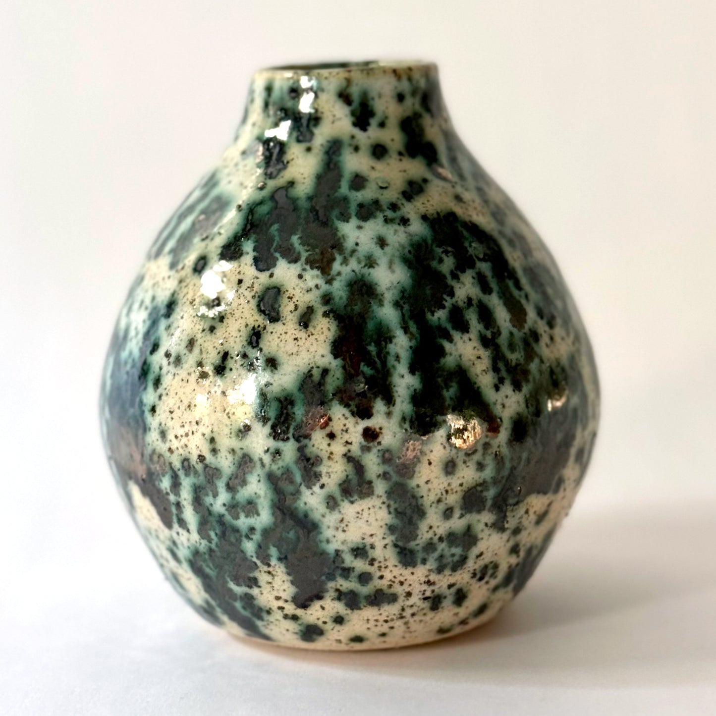 Small handmade pottery vase with a rounded shape and narrow opening, finished in a green jasper glaze with varied green tones and irregular speckled patterning across the surface.