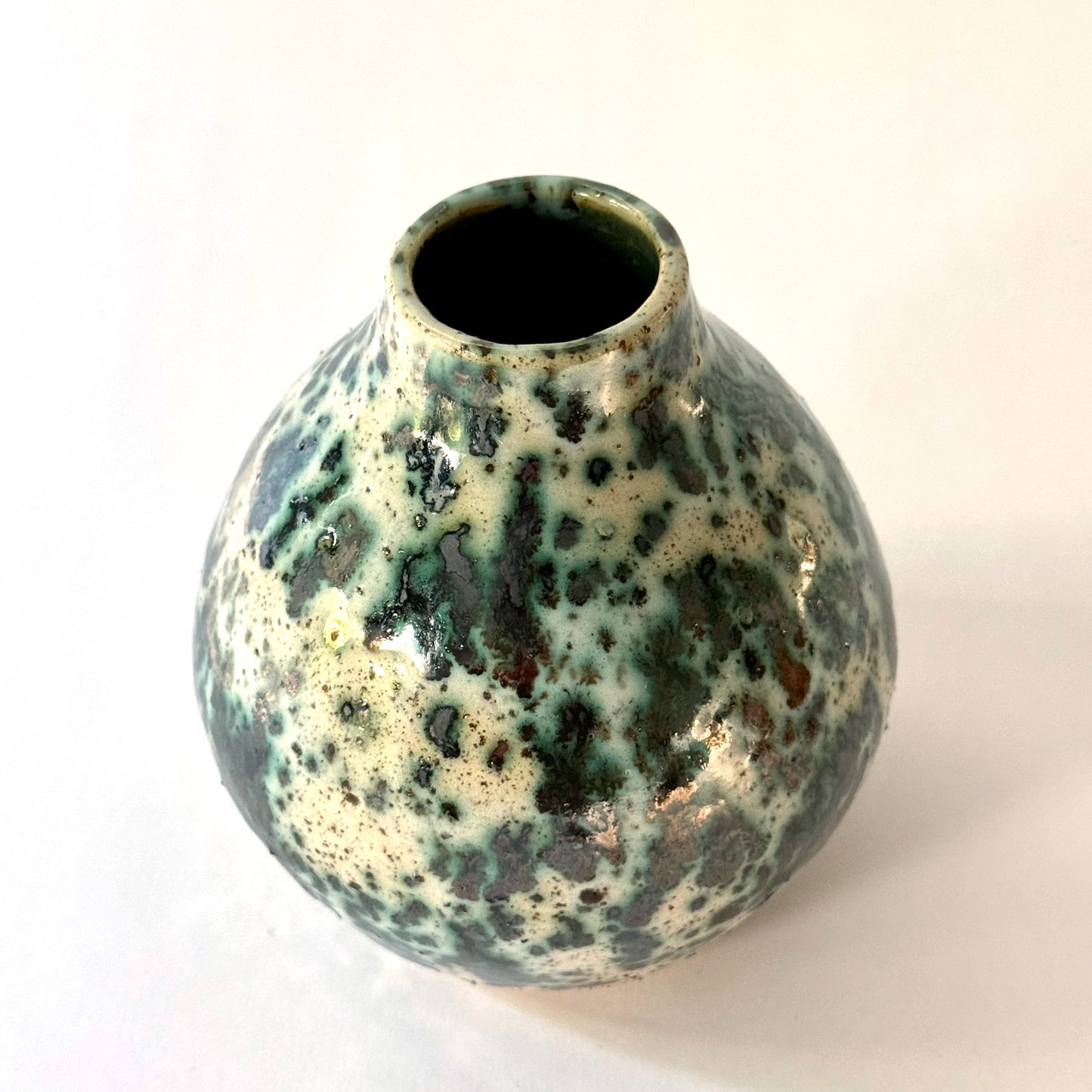 Small handmade pottery vase with a rounded shape and narrow opening, finished in a green jasper glaze with varied green tones and irregular speckled patterning across the surface.