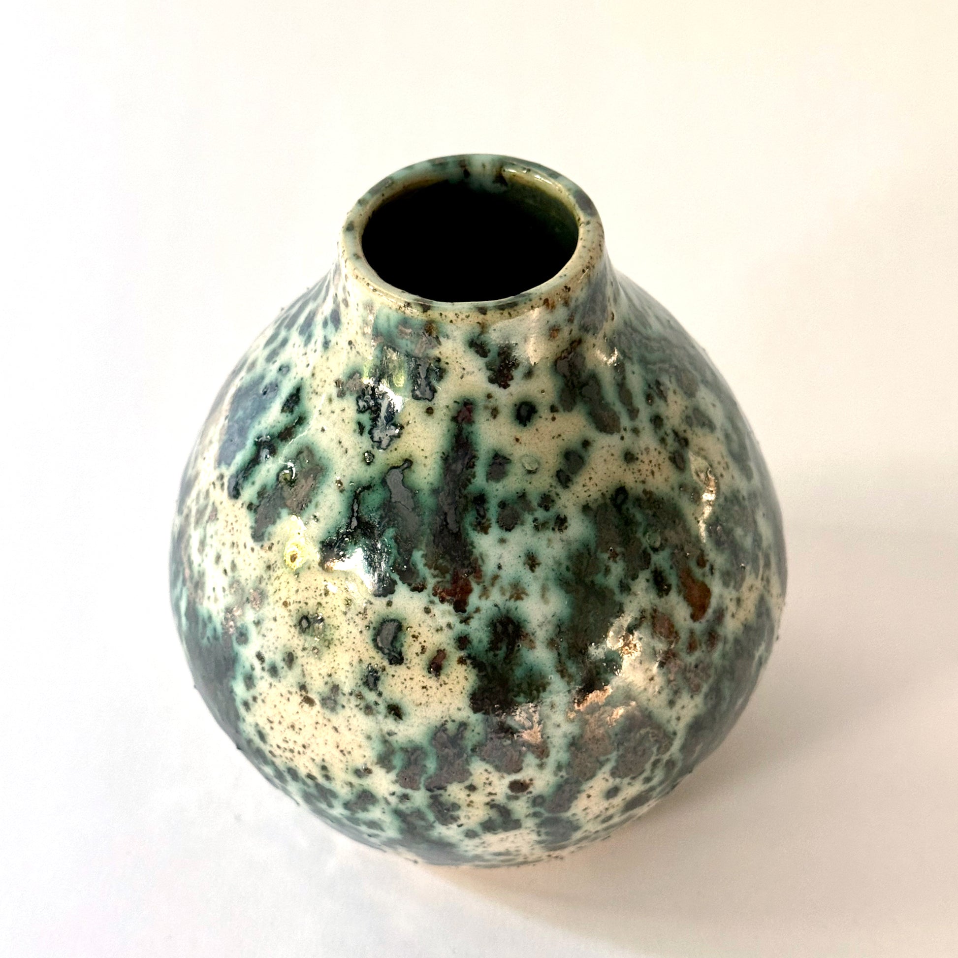 Small handmade pottery vase with a rounded shape and narrow opening, finished in a green jasper glaze with varied green tones and irregular speckled patterning across the surface.