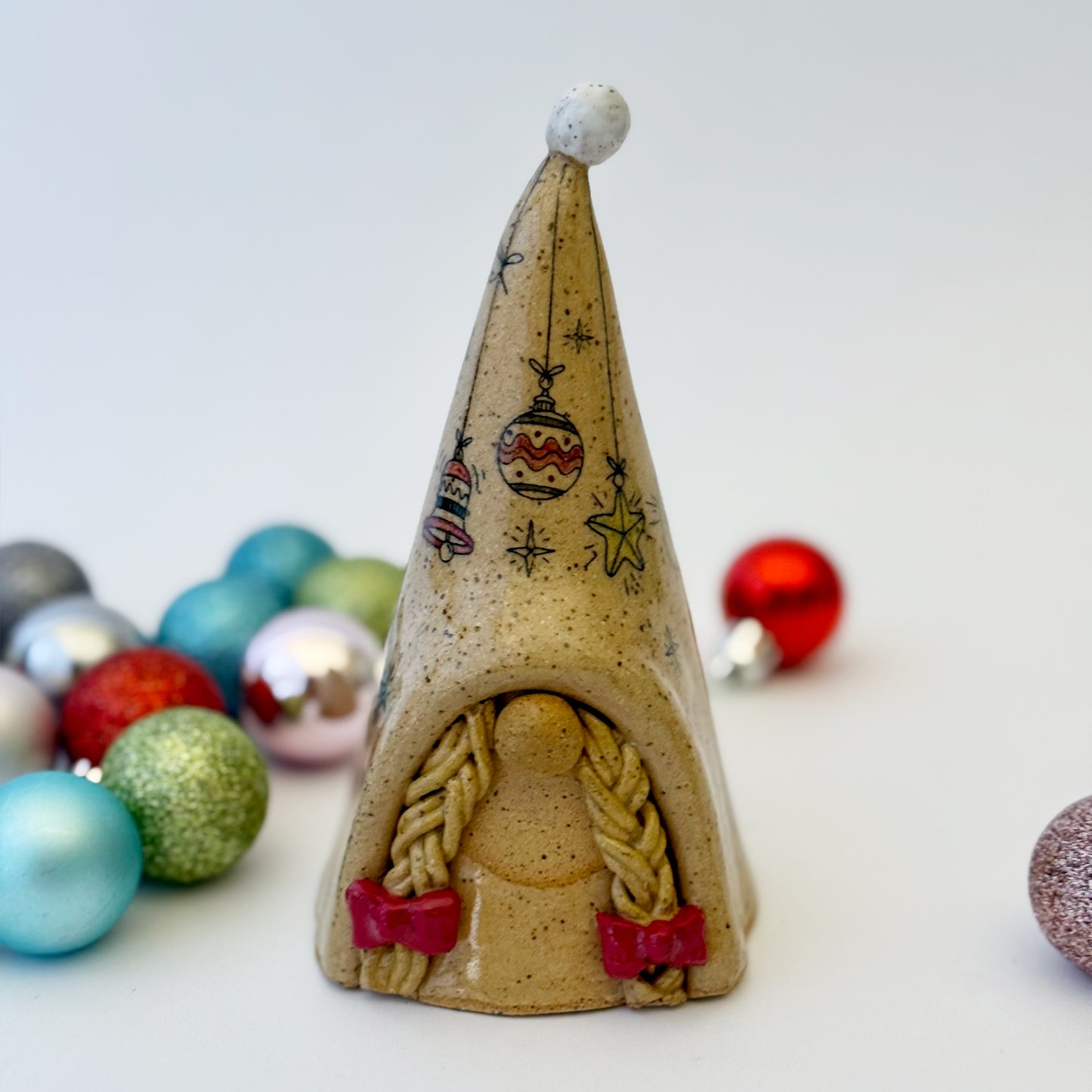 ceramic gnome with braids and red bows with ornaments on a white background 