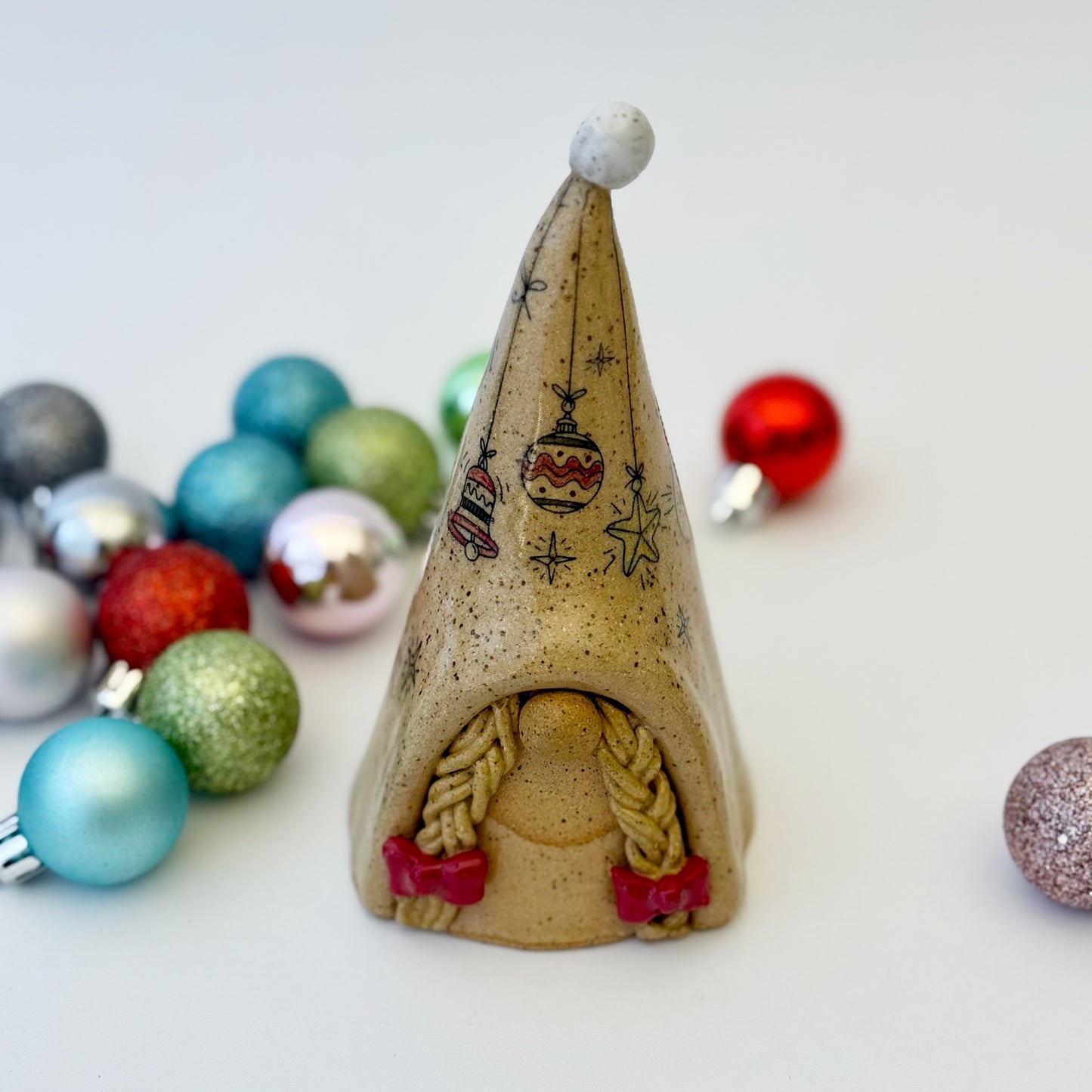 ceramic gnome with braids and red bows with ornaments on a white background 
