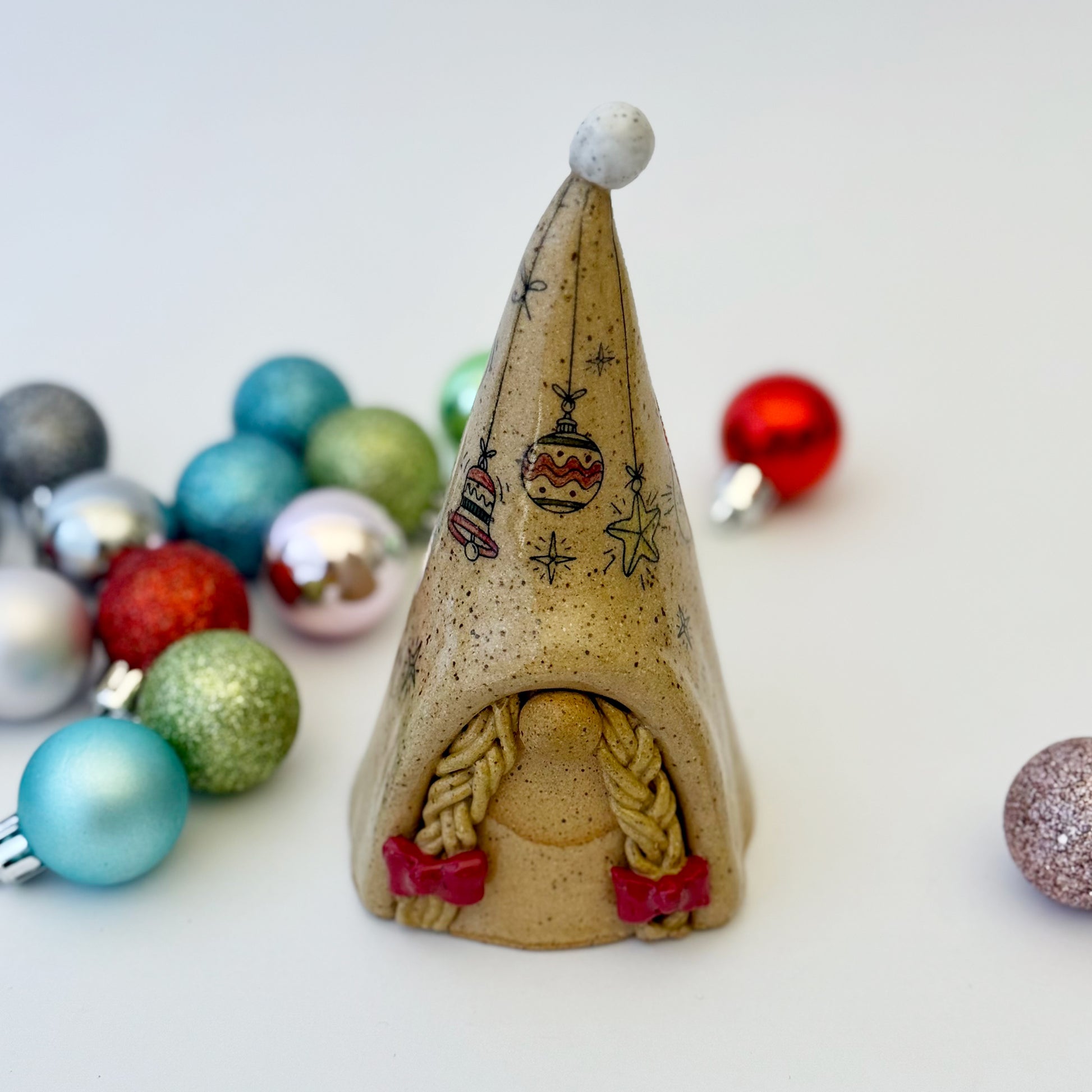 ceramic gnome with braids and red bows with ornaments on a white background 