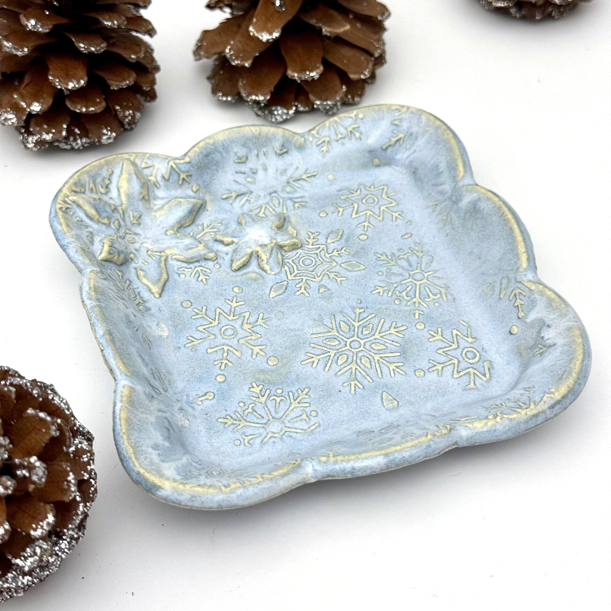 Decorative ceramic dish with snowflake patterns on a white background with pine cones.