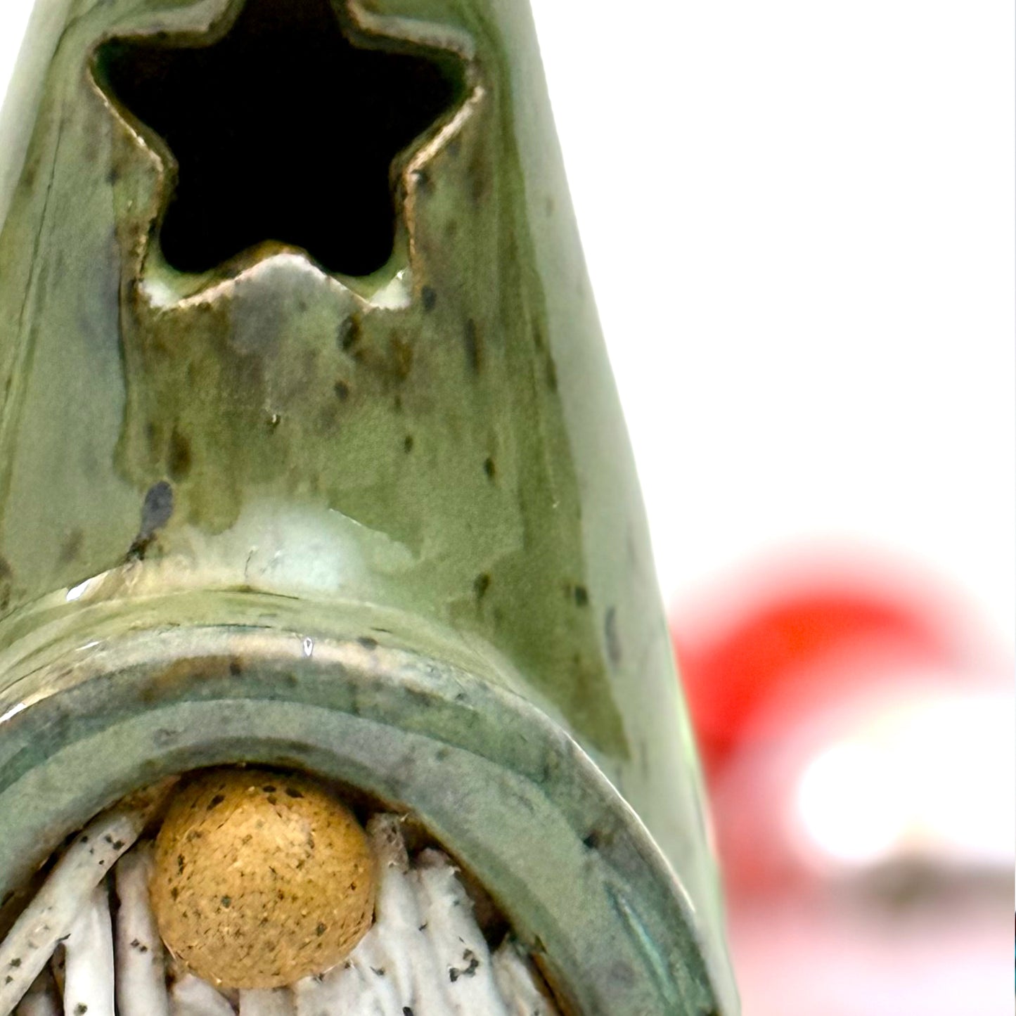 Close-up of a ceramic gnome luminary with a green hat, star-shaped window, speckled white beard, and round nose, styled with Christmas ornaments.