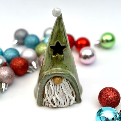A ceramic gnome luminary with a green hat, star-shaped window, speckled white beard, and round nose, styled with Christmas ornaments.