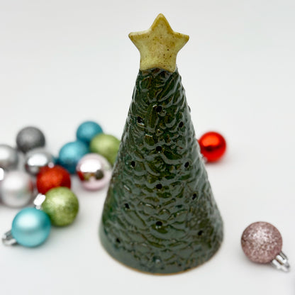 Green ceramic Christmas tree luminary with star on top, surrounded by colorful ornaments on a white background