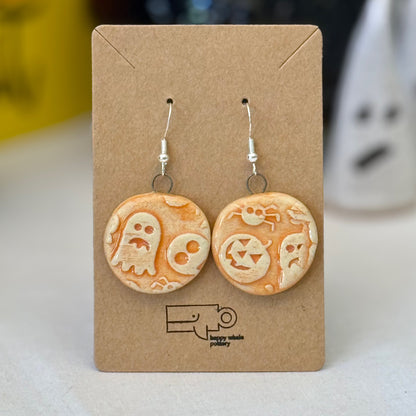 Pair of orange halloween themed ceramic earrings on a brown card with a blurred background