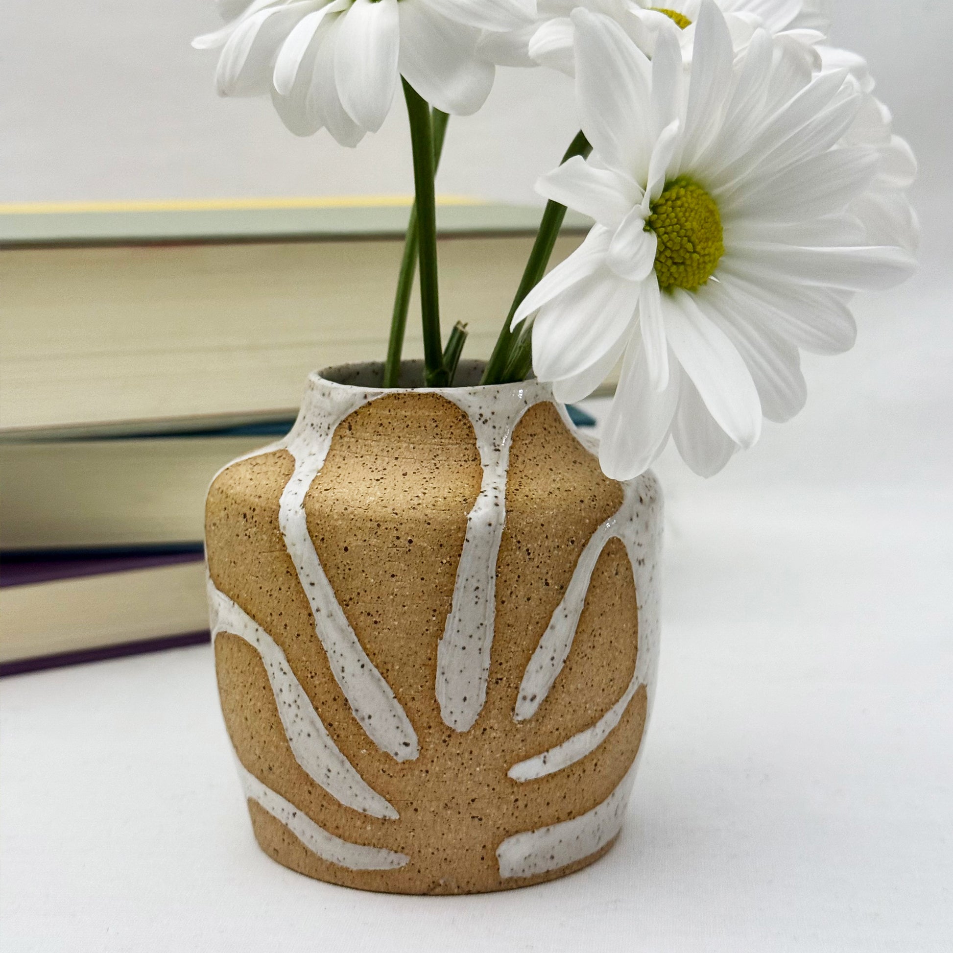 Ceramic vase with leaf patterns holding white flowers on a light background