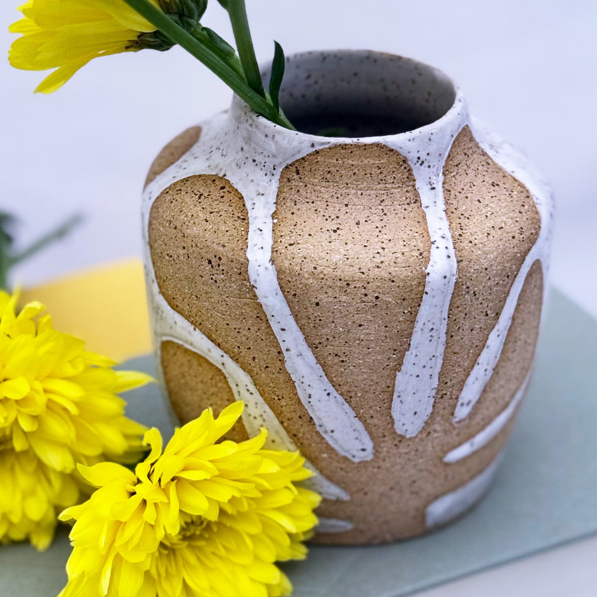 Ceramic vase with white glaze and yellow flowers on a light background