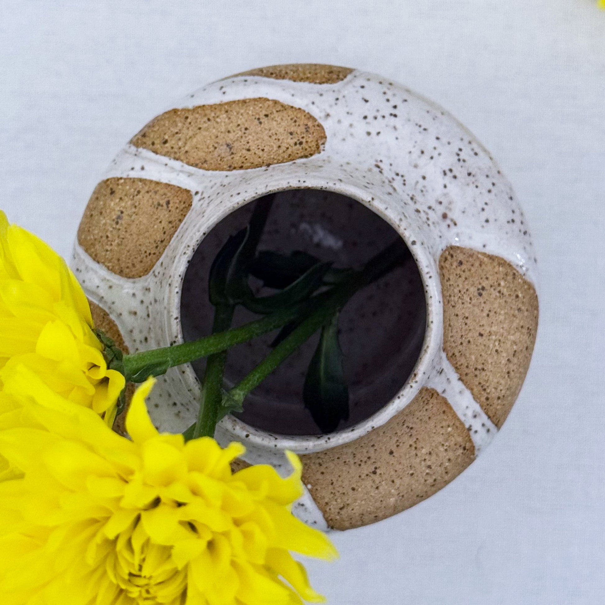 Speckled ceramic vase with yellow flowers on a light background