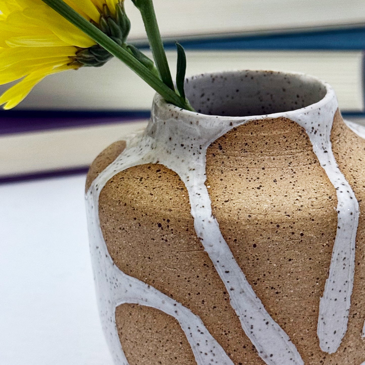 Ceramic vase with abstract design and a yellow flower on a blurred background