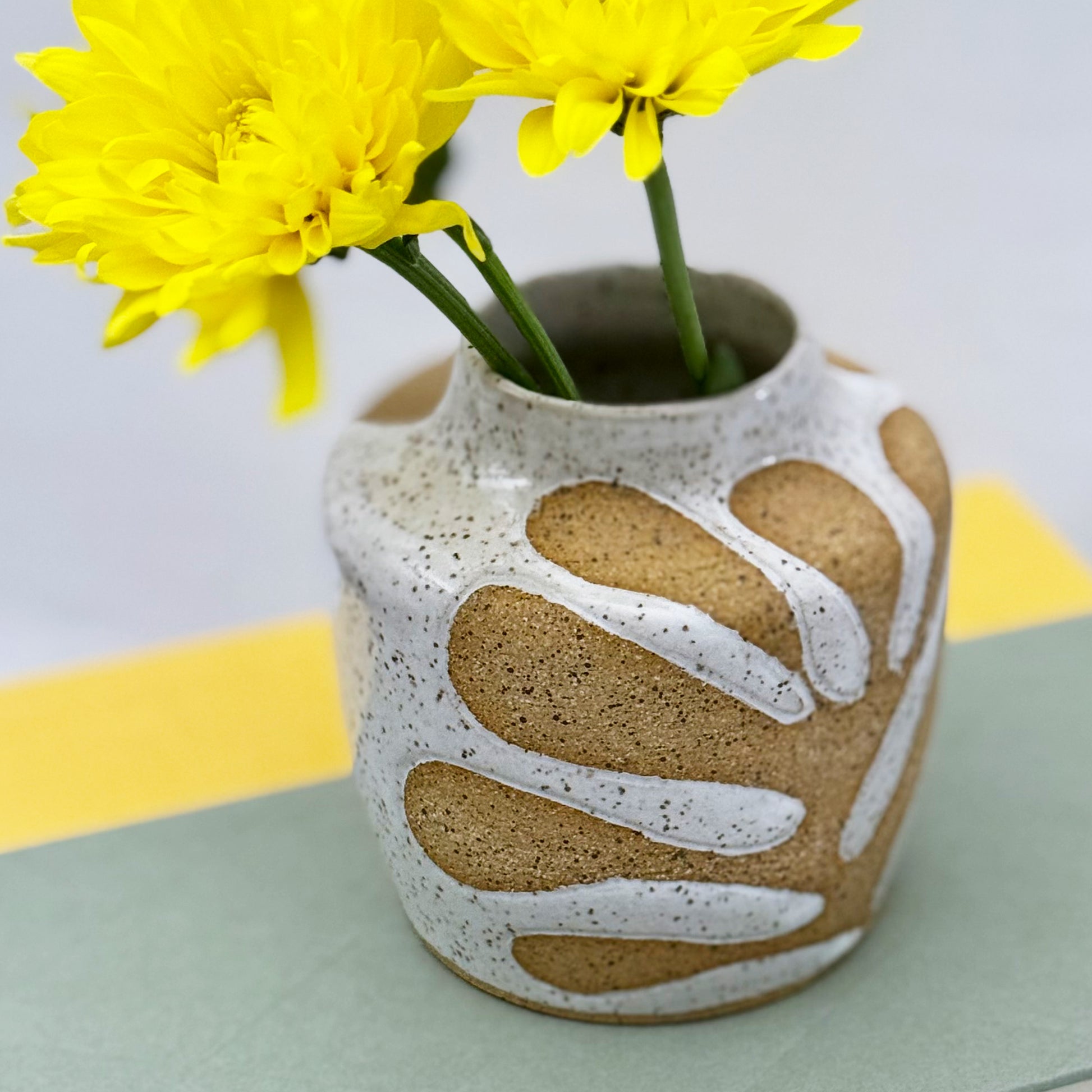 Decorative vase with leaf patterns and yellow flowers on a light background