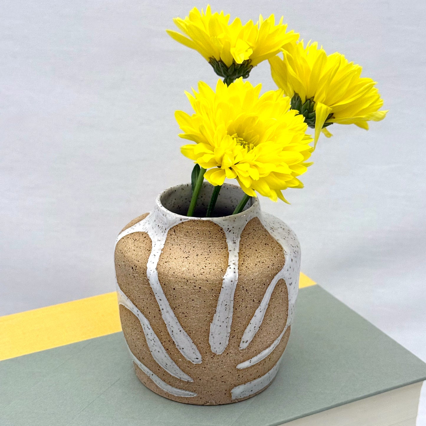 Ceramic vase with leaf patterns holding yellow flowers on a light background