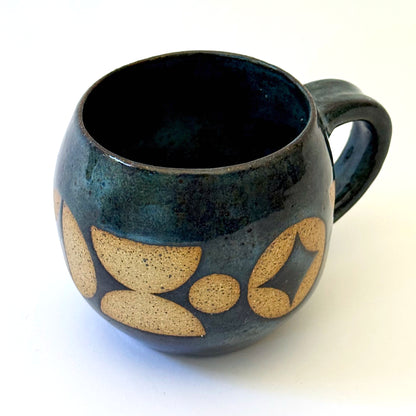 Ceramic mug with a rounded shape and handle, featuring an isometric geometric pattern revealed through a deep blue glaze.