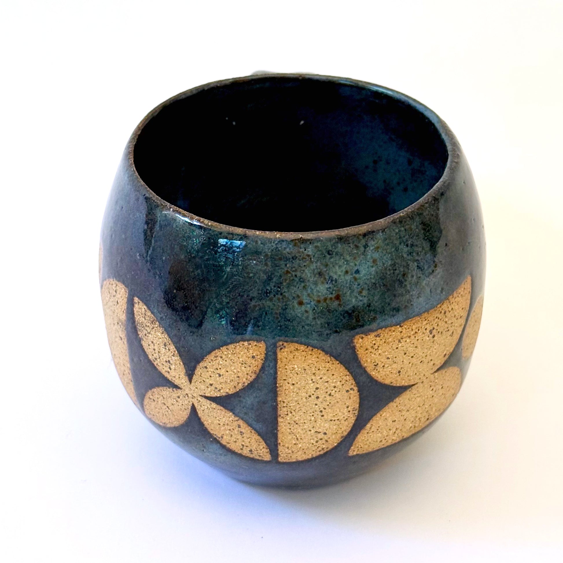 Ceramic mug with a rounded shape and handle, featuring an isometric geometric pattern revealed through a deep blue glaze.