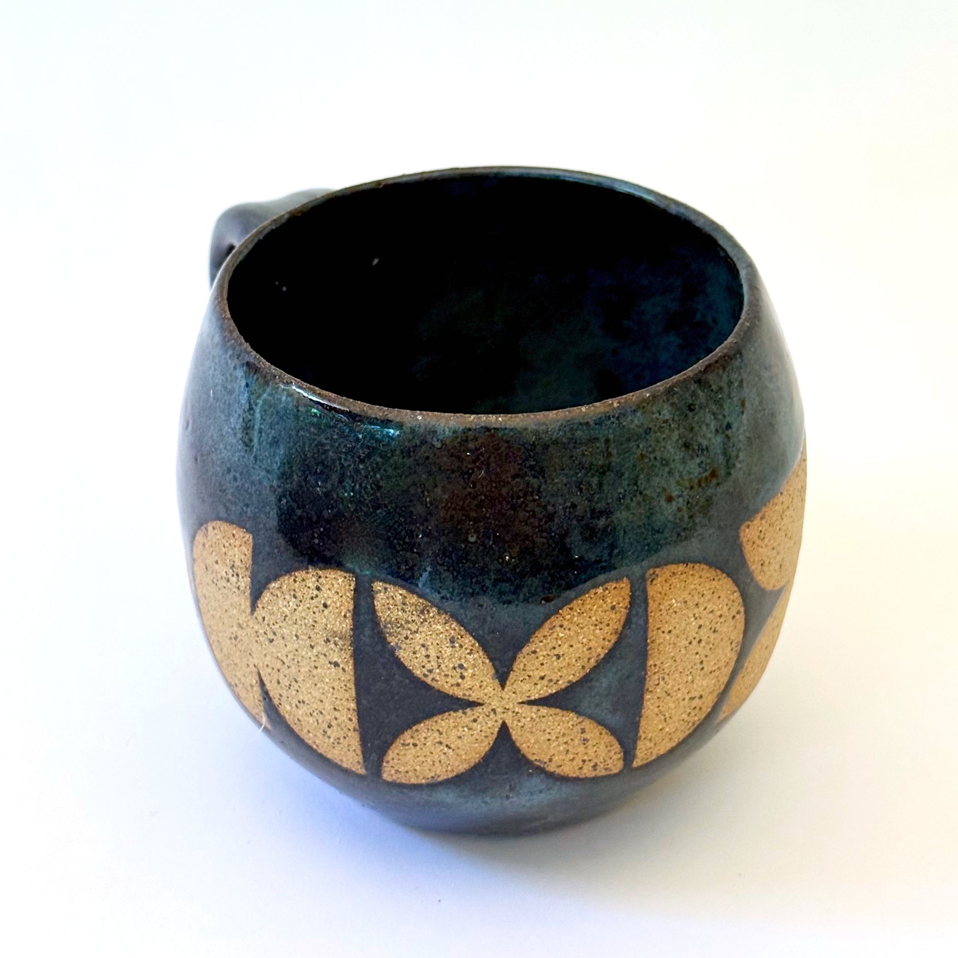 Ceramic mug with a rounded shape and handle, featuring an isometric geometric pattern revealed through a deep blue glaze.