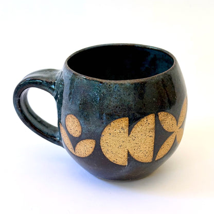 Ceramic mug with a rounded shape and handle, featuring an isometric geometric pattern revealed through a deep blue glaze.