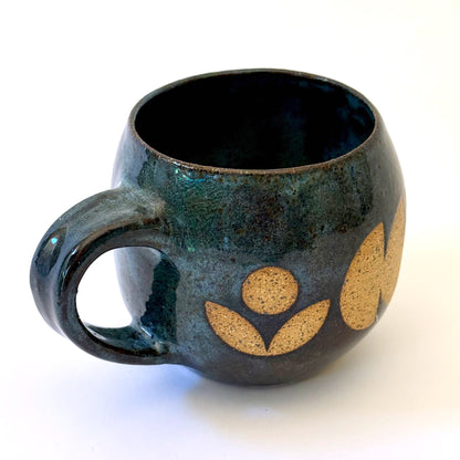 Ceramic mug with a rounded shape and handle, featuring an isometric geometric pattern revealed through a deep blue glaze.