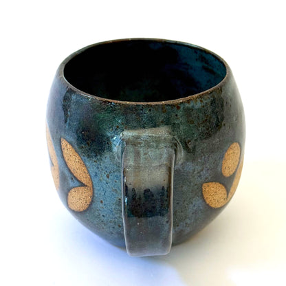 Ceramic mug with a rounded shape and handle, featuring an isometric geometric pattern revealed through a deep blue glaze.