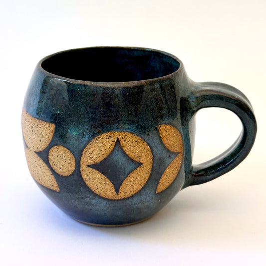 Ceramic mug with a rounded shape and handle, featuring an isometric geometric pattern revealed through a deep blue glaze.