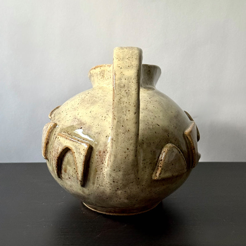 Small handmade stoneware jug with a rounded body, arched handle, curved spout, and raised mid-century geometric design, finished in a warm cream glaze.