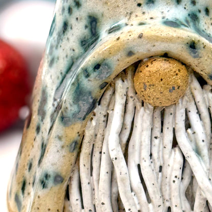 Close-up of a decorative gnome figure with a speckled hat surrounded by colorful ornaments on a white background