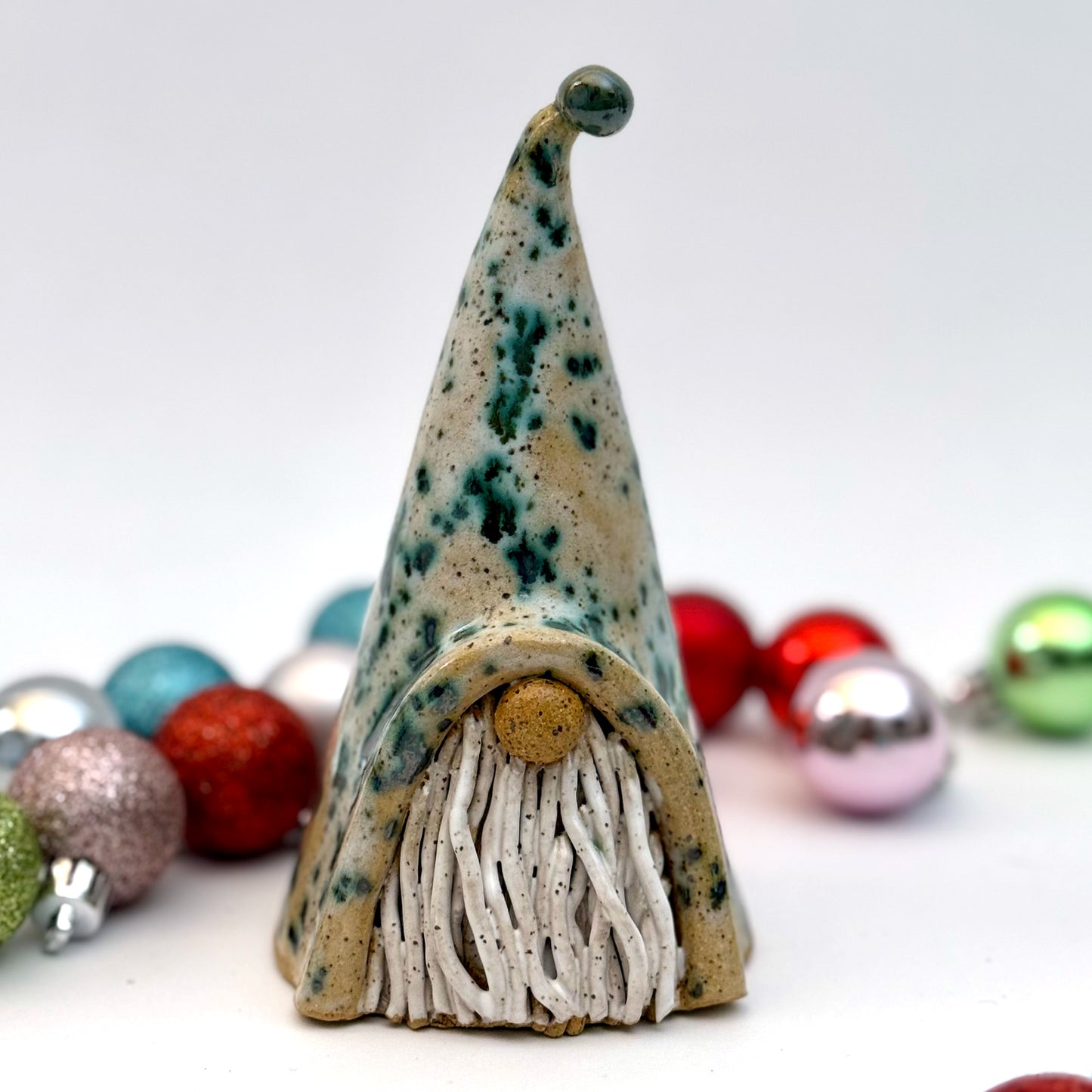 Decorative gnome figure with a speckled hat and beard, surrounded by colorful ornaments on a white background.