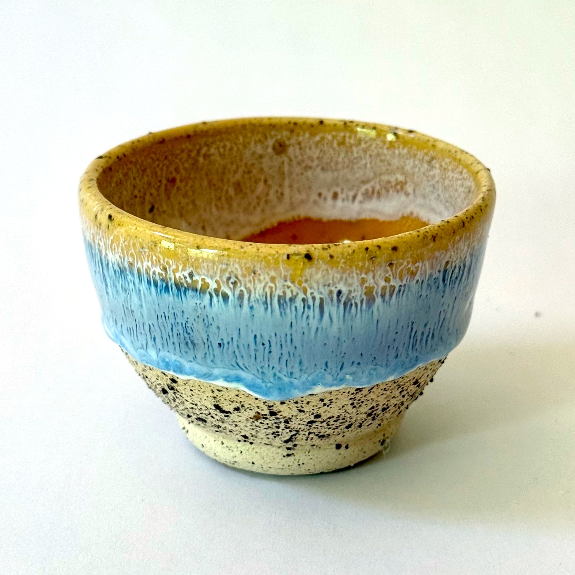 Small handmade ceramic bowl with a pedestal base, featuring a golden rim that transitions into a light blue glaze over speckled stoneware.