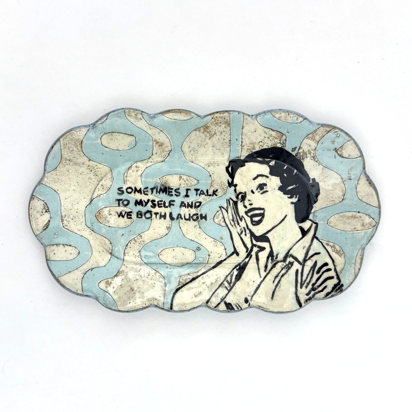 Handmade scalloped-edge ceramic plate with a retro illustrated woman, blue and cream mid-century geometric pattern, and the phrase “Sometimes I talk to myself and we both laugh.”