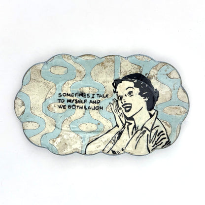 Handmade scalloped-edge ceramic plate with a retro illustrated woman, blue and cream mid-century geometric pattern, and the phrase “Sometimes I talk to myself and we both laugh.”