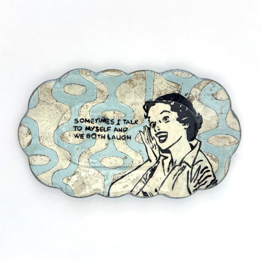 Handmade scalloped-edge ceramic plate with a retro illustrated woman, blue and cream mid-century geometric pattern, and the phrase “Sometimes I talk to myself and we both laugh.”