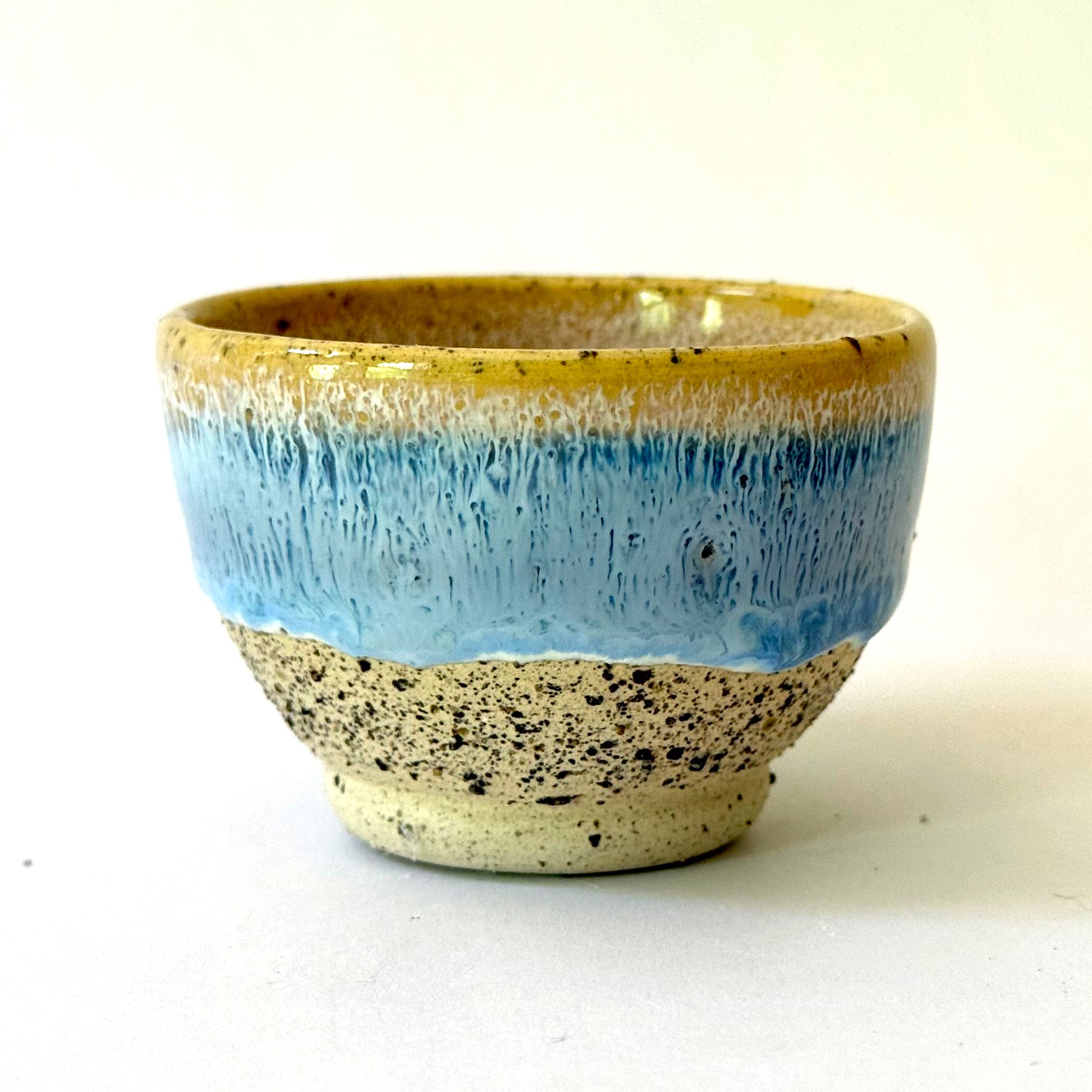 Small handmade ceramic bowl with a pedestal base, featuring a golden rim that transitions into a light blue glaze over speckled stoneware.