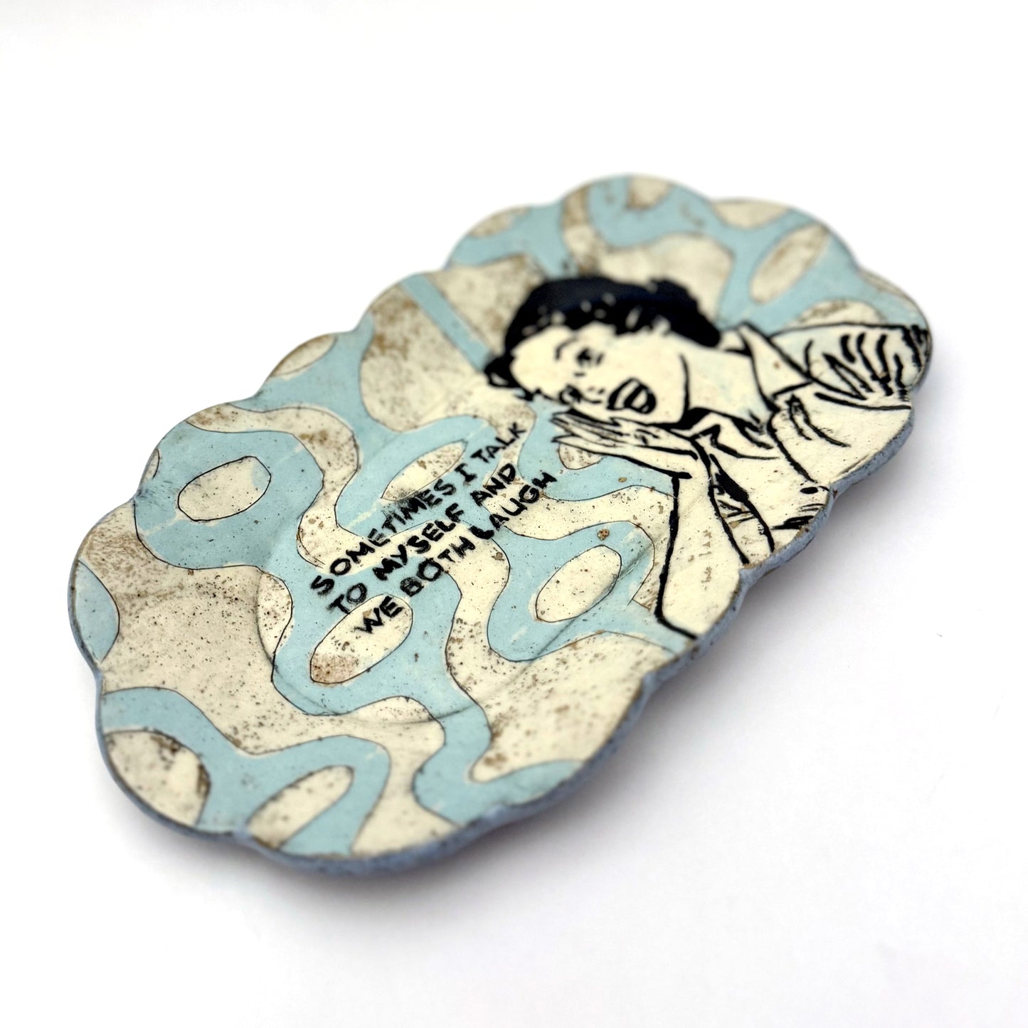 Handmade scalloped-edge ceramic plate
 with a retro illustrated woman, blue and cream mid-century geometric pattern, and the phrase “Sometimes I talk to myself and we both laugh.”