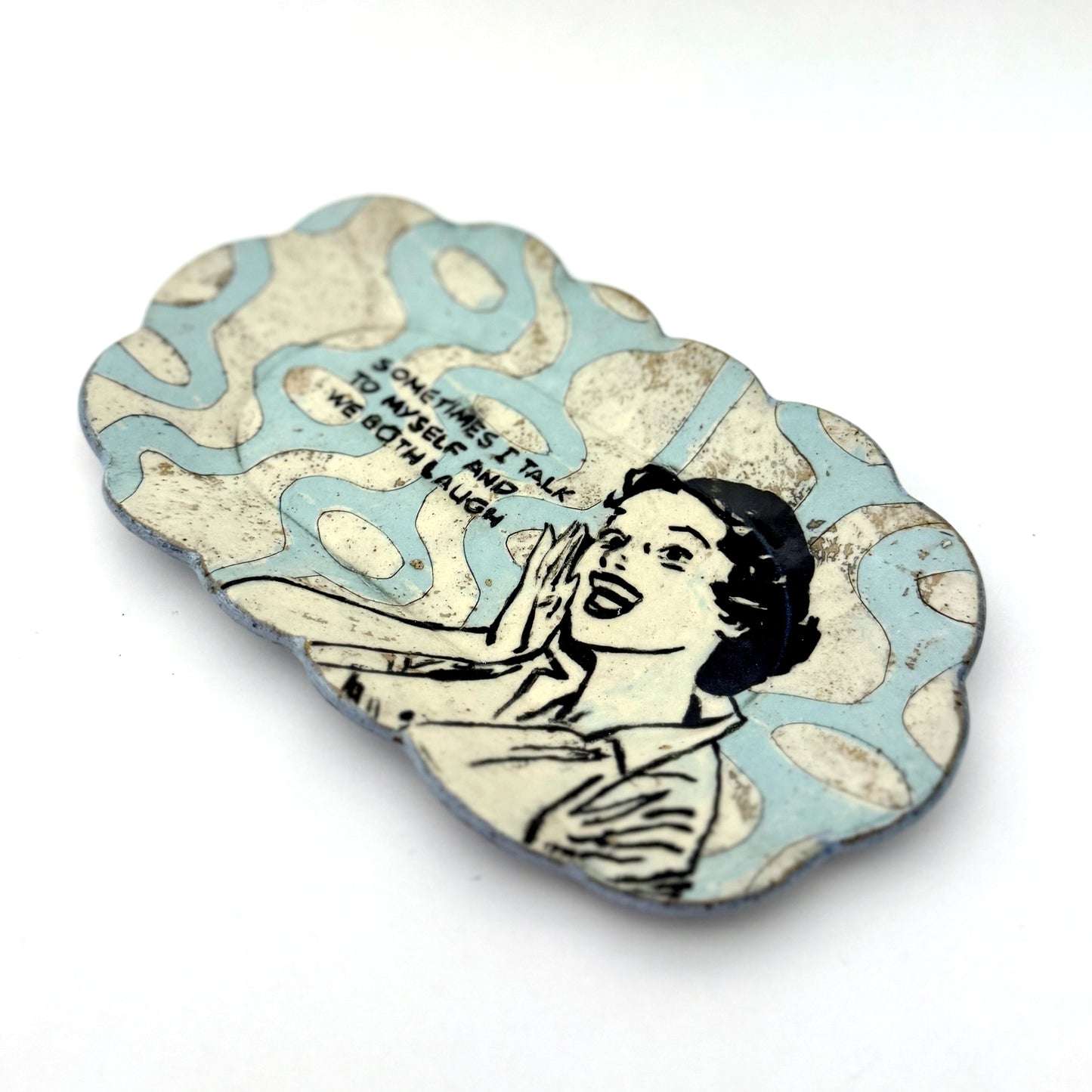 Handmade scalloped-edge ceramic plate with a retro illustrated woman, blue and cream mid-century geometric pattern, and the phrase “Sometimes I talk to myself and we both laugh.”