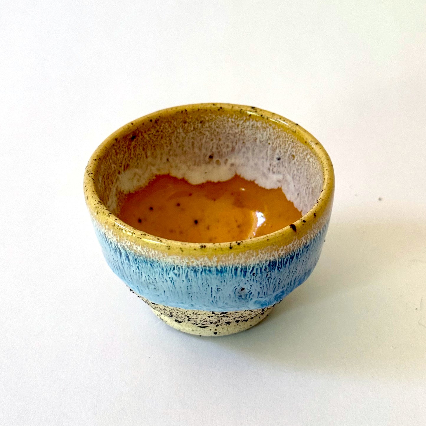 Small handmade ceramic bowl with a pedestal base, featuring a golden rim that transitions into a light blue glaze over speckled stoneware.