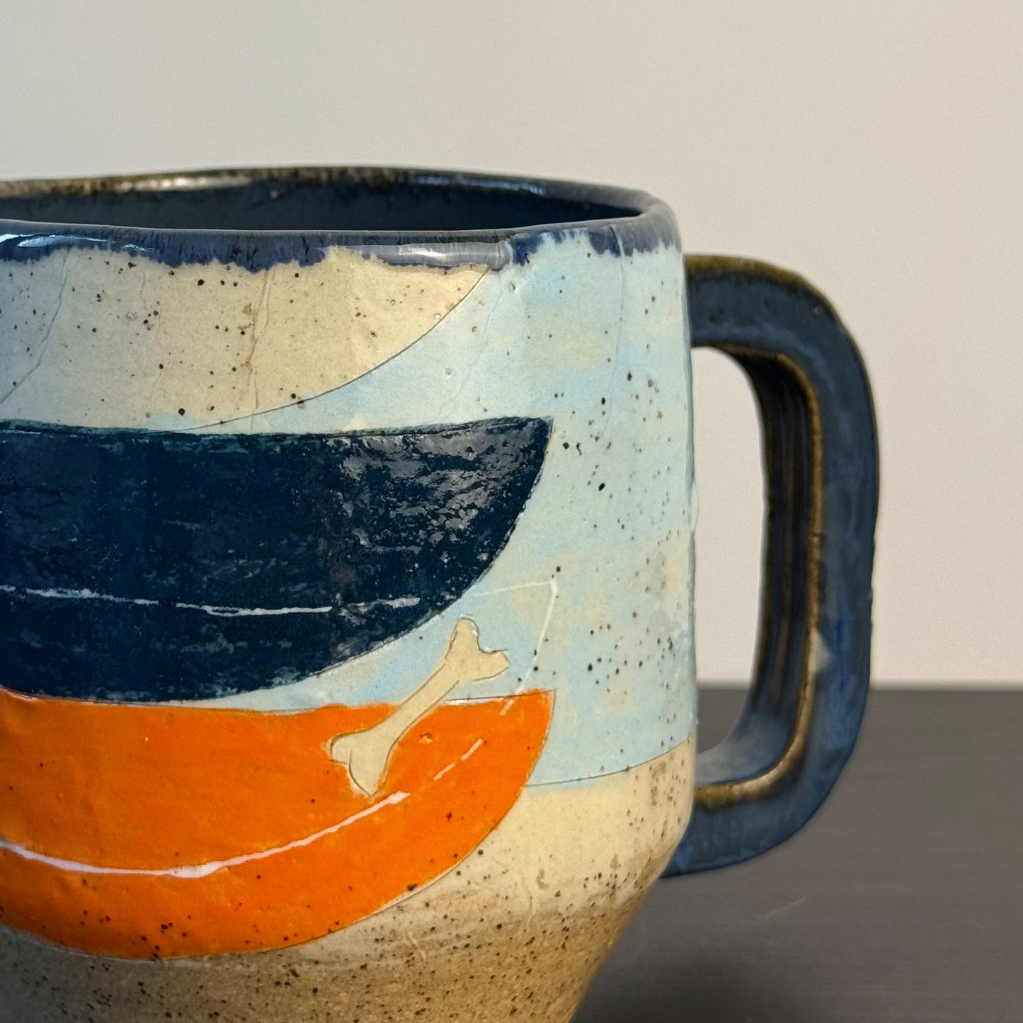 Handcrafted mid-century modern ceramic mug featuring a black dachshund dog, atomic starbursts, and retro geometric patterns in orange and light blue with a raw stoneware base.