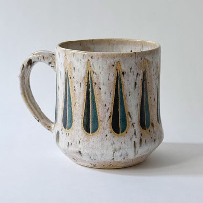 Handmade stoneware mug with a teal-and-black teardrop pattern on a speckled cream glaze, photographed against a white background.
