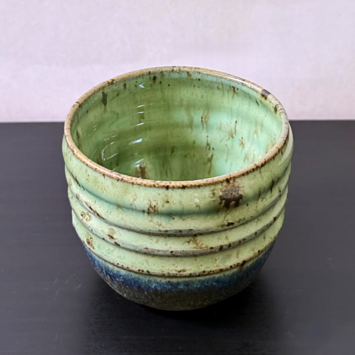 Small handmade Olive Groove Pot with a rounded shape, carved horizontal bands, and glossy olive-green glaze that shifts to deep blue-green and earthy brown near the base.