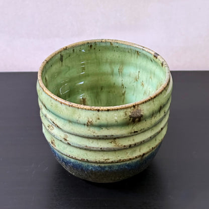 Small handmade Olive Groove Pot with a rounded shape, carved horizontal bands, and glossy olive-green glaze that shifts to deep blue-green and earthy brown near the base.